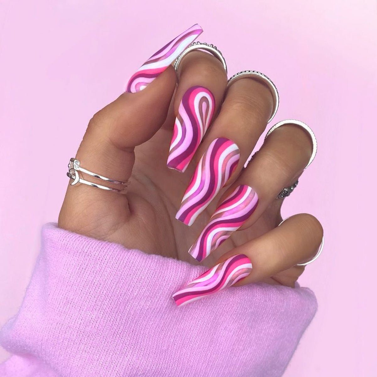 Hand with pink and white wavy nail art on a pink background
