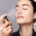 Person holding a spray bottle near their face against a neutral background