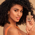 Woman holding a bottle of foundation against a beige background