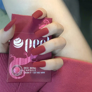 Hand holding a pink box labeled 'Red Wine' with red nail polish.