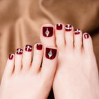 Close-up of feet with red nail polish and diamond decorations on a brown background