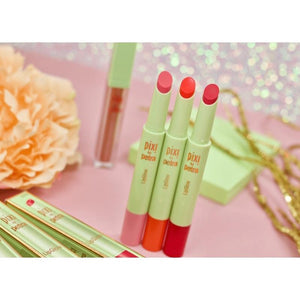 Three lipsticks with red caps on a pink surface with decorative elements