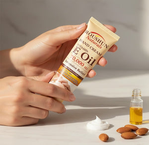Hand holding a Roushun Naturals Vitamin E Oil hand cream with almonds and oil on a light surface.