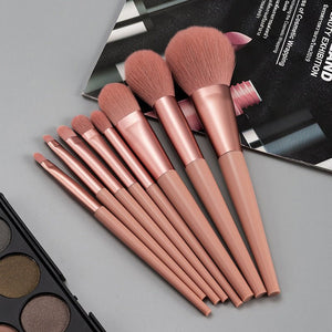 Set of makeup brushes with rose gold handles on a gray surface.
