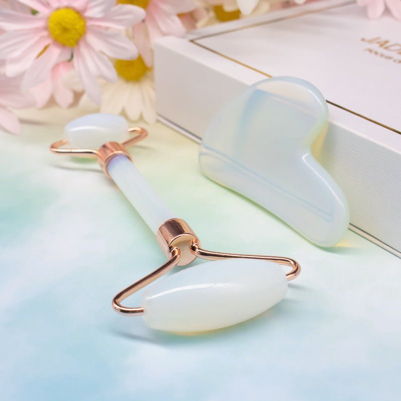Two jade rollers with rose gold accents on a light blue surface with flowers in the background.