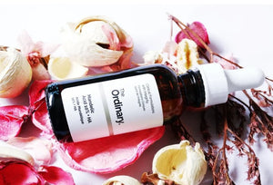 The Ordinary skincare serum bottle on a decorative background with flowers and seashells