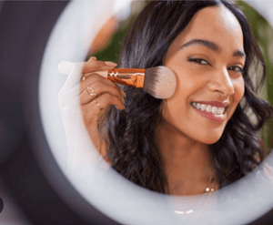 Woman applying makeup with a brush in front of a circular mirror