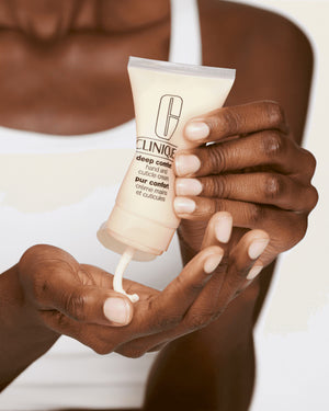 Person holding a tube of Clinique hand cream with visible cream being squeezed out.