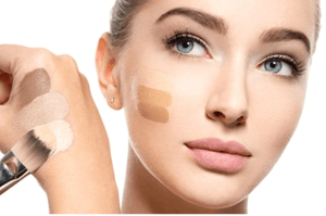 Woman applying makeup with a brush on her face, showcasing different shades.