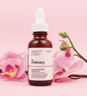 The Ordinary skincare serum bottle with pink orchids on a light pink background