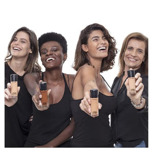 Four women holding up bottles of foundation against a white background