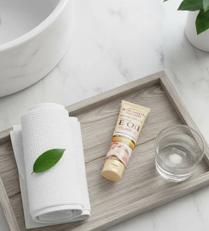 Bathroom setting with a towel, bottle, and glass on a wooden tray.