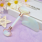 Jade roller and gua sha tool on a purple surface with flowers and a box in the background.
