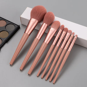 Set of rose gold makeup brushes on a gray surface with a makeup palette in the background.
