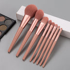 Set of rose gold makeup brushes on a gray surface with a makeup palette in the background.