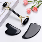 Black gua sha tools on a white surface with pink flowers and a box.
