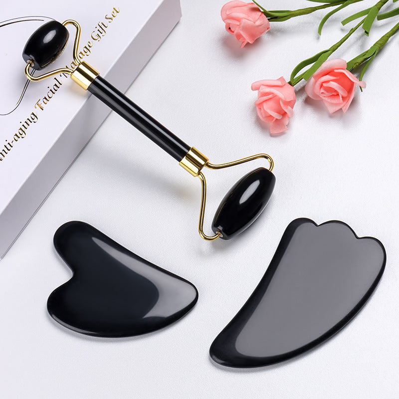 Black gua sha tools on a white surface with pink flowers and a box.