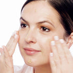 Woman applying a skincare product to her face with a white background