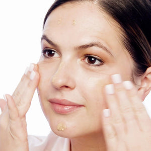 Woman applying a skincare product to her face with a white background