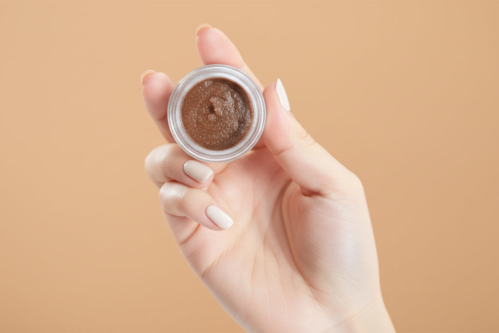 Hand holding a small container of brown powder against a beige background