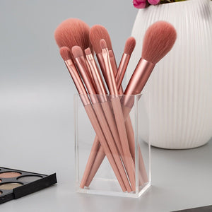 Set of rose gold makeup brushes in a clear holder on a light gray background