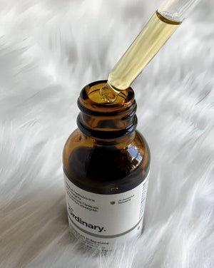 Brown glass bottle with dropper labeled 'The Ordinary' on a white fur background
